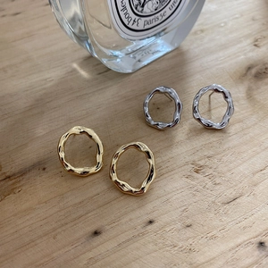 Detailed view of gold and silver irregular wave stud earrings on a wooden texture