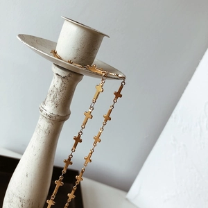 Detailed view of a gold-plated cross choker necklace hung on a white vintage candle holder