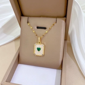 Gold square pendant necklace with green heart gem and shell inlay in a beige jewelry box