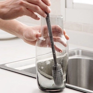 Long-handle silicone cleaning brush scrubbing a transparent glass bottle in a kitchen sink