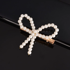 Close-up of handmade woven bow hair clip with white pearls on a black reflective surface