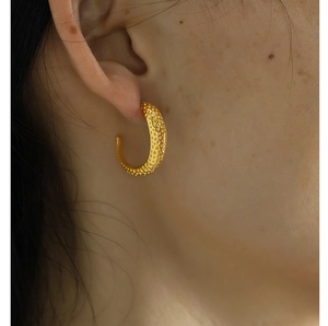 Close-up of golden C-shaped stud earrings with textured surface worn by a model