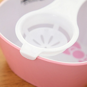 White plastic egg white separator tool placed on a pink bowl over a wooden table