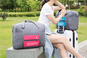 Grey travel storage bag on a suitcase handle featuring pink and blue zipper pockets