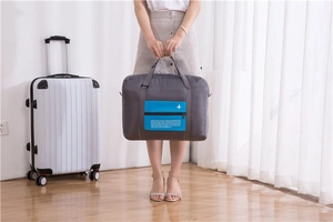 Detail of grey foldable travel bag with blue pocket and logo on white suitcase handle