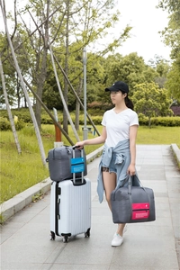Travel folding storage bag attached to suitcase handle in gray and pink colors