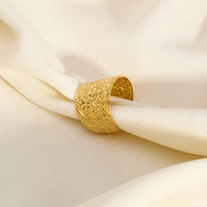 Close-up of hammered 18K gold plated wide ring resting on elegant white silk fabric