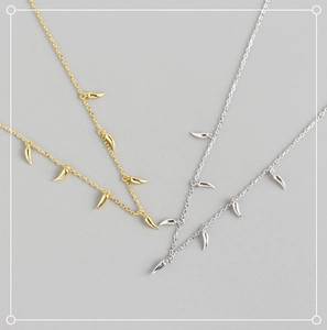 Detail of silver and gold S925 necklaces with minimalist horn charms on a grey surface