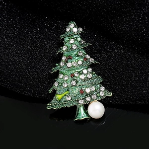 Green Christmas tree brooch with white rhinestones and a pearl on dark fabric background