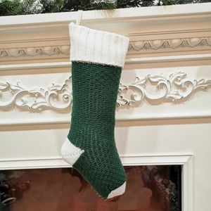 Close-up of green and white knit Christmas stocking hanging on a white fireplace