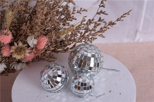 Three silver mirror disco balls in various sizes on white base with dried flowers decor