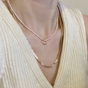 Layered gold chain necklace with round pendant and white pearl strand on model