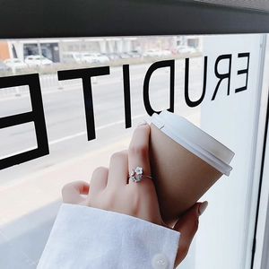 Close-up of a silver flower ring with white petals and blue crystals held against a cup
