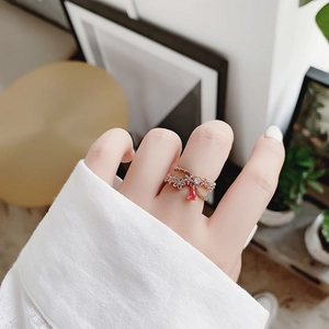 Close-up of a rose gold flower ring with red teardrop gem worn by a model in soft light