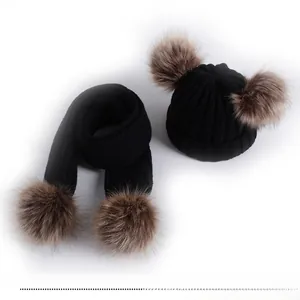 Detail of black winter knitted hat and scarf set featuring brown faux fur pom-poms