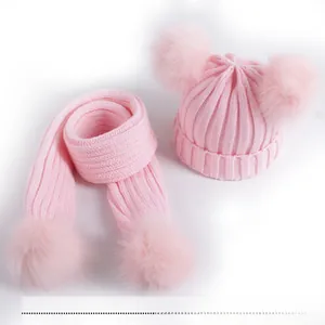 Detailed view of pink ribbed knit children hat and scarf set with soft faux fur pom-poms