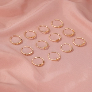 Detail view of twelve gold zodiac letter rings set on a soft pink silk fabric background