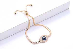 Detail van gouden schakelarmband met blauwe evil eye bedel en verstelbare schuifsluiting