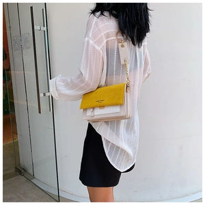 Detail of yellow and beige contrast shoulder bag with metal chain strap on model