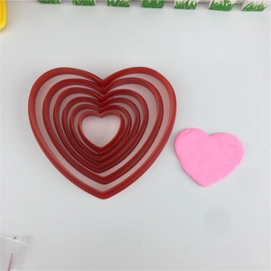 Nesting set of red heart-shaped plastic cookie cutters with pink heart sample on white surface