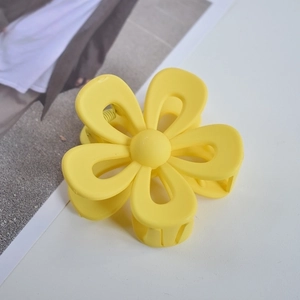 Close-up of a matte yellow flower-shaped hair claw clip on a clean white desk surface