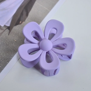 Detail view of large purple matte flower hair claw clip on a minimalist white surface