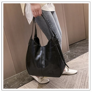 Detailed view of large black soft leather tote bag worn by a model in a casual indoor setting