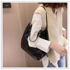 Close-up of black leather tote bag with embossed logo worn by model in casual outfit