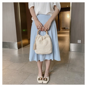 Detail of cream straw bucket bag with wooden ring handle and stylish tassel accent