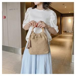 Detail of woven straw handbag featuring a smooth round wooden handle and tassel accent