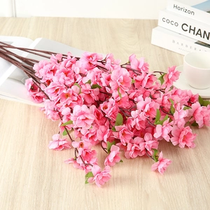 Detailed view of pink artificial silk roses on light wood table with books and coffee cup