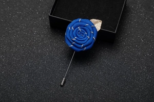 Macro detail of blue fabric rose brooch with golden leaves and metal lapel pin