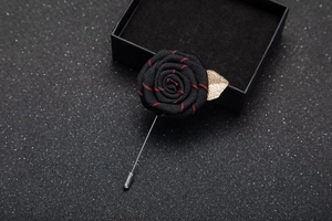 Macro shot of black rose fabric boutonniere with golden metal leaf detail and silver pin