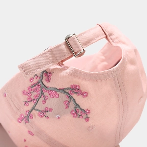 Detail of pink cotton baseball cap featuring floral embroidery and silver metal buckle