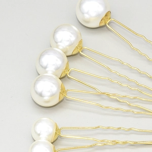 Detailed macro view of U-shaped bridal hair pins with white pearls and gold finish