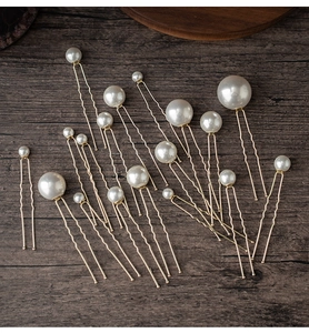 Detail of assorted white pearls on golden U-shaped hairpins over a vintage wood background