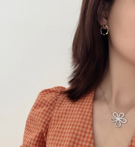 Close-up of irregular gold-plated hoop earrings worn with a floral pendant necklace