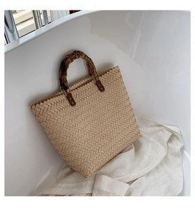 Détail d'un sac cabas en paille tressée avec poignée en bambou et attaches en cuir