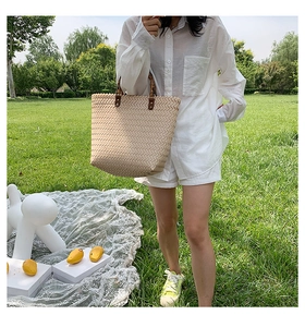 Détail du sac seau en paille tressée beige avec poignées en bambou et attaches en cuir