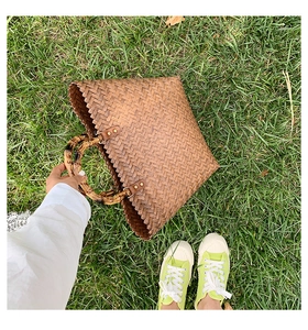 Détail du sac cabas tressé avec poignées en bambou et texture marron sur l'herbe