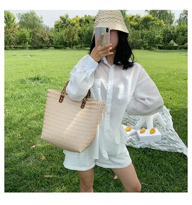 Gros plan d'un sac cabas tissé beige avec texture en V et poignées en cuir sur l'herbe