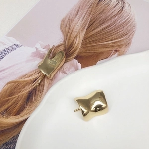 Close-up of golden irregular geometric hair clip with polished finish on a white plate