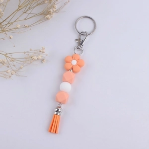 Detailed view of orange silicone beads, flower charm, and tassel keychain on white background