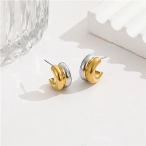 Minimalist two-tone gold and silver C-shaped hoop earrings on elegant aesthetic props