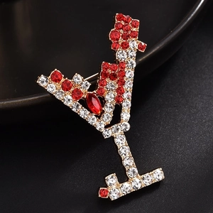 Close-up of golden cocktail glass brooch with red oval gemstone and sparkling rhinestones
