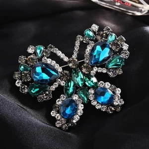 Macro shot of a butterfly brooch with vibrant blue-green crystals on dark silk fabric