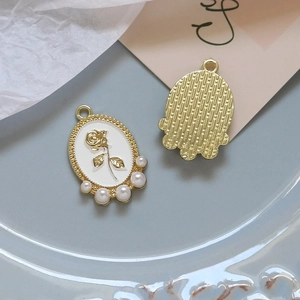 Detail of rose embossed alloy charms with white enamel and pearl accents for DIY jewelry
