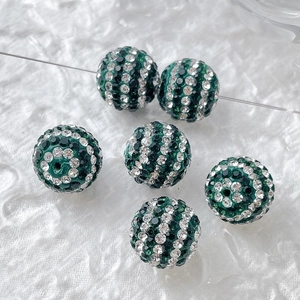 Detail of spherical beads with green and white rhinestones on white fabric background