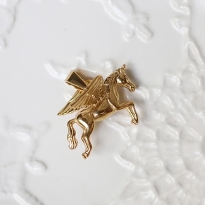 Macro shot of 18K gold plated Pegasus pendant with detailed wings on white surface