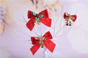 Detail of red Christmas bows with golden bells and green holly leaves on white stand